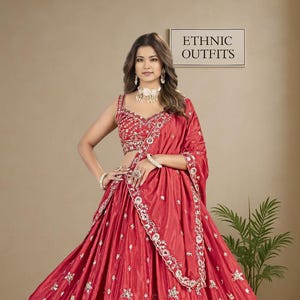 May include: A striking red ethnic outfit, with a detailed skirt and matching top, embellished with gold embroidery. The outfit includes a draped shawl and is labelled "ETHNIC OUTFITS".