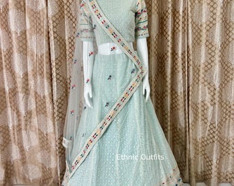 May include: A light blue ethnic outfit, comprising a top, skirt, and scarf, presented on a mannequin. The outfit showcases detailed embroidery with vibrant floral designs. The text "Ethnic Outfits" is displayed on the skirt.