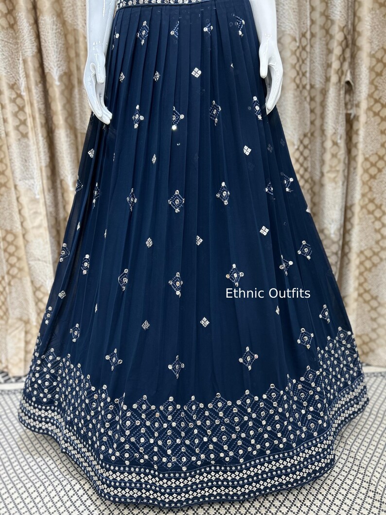 May include: Navy blue pleated skirt with intricate silver embroidery. The skirt features a detailed geometric pattern along the hemline and scattered diamond-shaped embellishments. The text "Ethnic Outfits" is visible on the image.