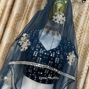 May include: A dark teal ethnic outfit, including a top and veil, displayed on a mannequin. The top is embellished with sequins and silver embroidery. The veil is sheer and adorned with decorative silver accents. The text "Ethnic Outfits" is visible.