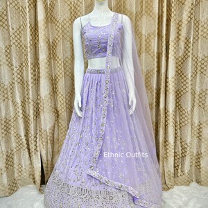 May include: A lilac lehenga choli set with detailed silver embroidery. The set comprises a crop top, a long skirt, and a matching dupatta. The text "Ethnic Outfits" is visible on the dupatta.