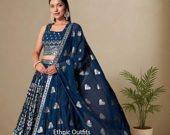Puede incluir: Una mujer con un atuendo étnico azul marino. El atuendo incluye un top sin mangas y una falda larga, ambos con patrones plateados. Una bufanda a juego cae sobre el hombro. El atuendo está etiquetado como "Ethnic Outfits".