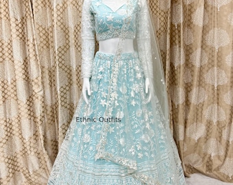 Puede incluir: Un lehenga azul claro con intrincados bordados florales blancos. El conjunto incluye una blusa a juego con mangas largas y un dupatta transparente. El texto "Ethnic Outfits" es visible en la falda. El atuendo se muestra en un maniquí.