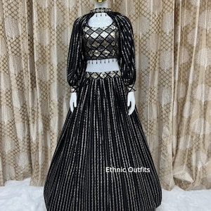 May include: Black and gold ethnic outfit displayed on a mannequin. The outfit includes a crop top, long skirt, and a jacket with vertical silver stripes. The crop top has a diamond pattern. The skirt is floor-length. The text "Ethnic Outfits" is visible.