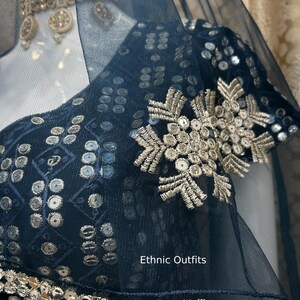May include: Close-up of a navy blue ethnic outfit with intricate silver embroidery and sequin detailing. The outfit features a sheer overlay and the text "Ethnic Outfits". The design includes floral and geometric patterns.