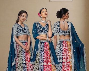 May include: Three women wearing colorful ethnic outfits. Each outfit includes a dark blue embroidered top, a multi-colored skirt, and a matching sheer scarf. The skirts feature a patchwork design with red, blue, green, and yellow panels. The sign in the background says "ETHNIC OUTFITS."