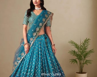 Puede incluir: Un conjunto étnico de color turquesa, con un top y una falda a juego, adornado con intrincados bordados plateados. El conjunto incluye un dupatta transparente y está etiquetado como "Ethnic Outfits".