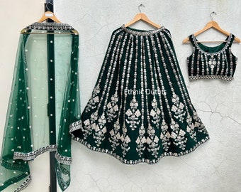 Op de afbeelding: Een groene en zilveren geborduurde lehenga met een bijpassende choli en dupatta. De lehenga heeft een uitlopende rok met een zilveren rand en een zilveren geborduurd ontwerp. De choli is mouwloos en heeft een ronde hals. De dupatta is doorschijnend en heeft een zilveren rand.