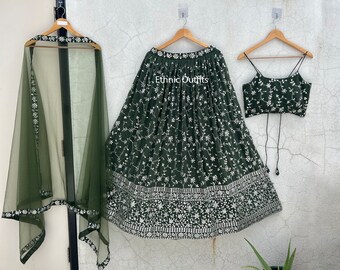 Op de afbeelding: Een donkergroene geborduurde rok met een wit bloemenpatroon, een bijpassend topje zonder mouwen en een doorschijnende groene dupatta. De rok heeft een witte zoom met een bloemenpatroon. De tekst "Ethnic Outfits" is zichtbaar op de rok.