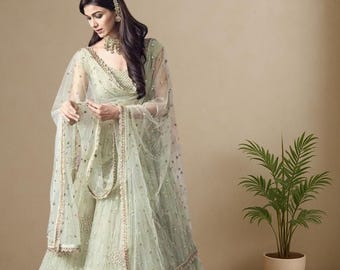 May include: A pale green ethnic outfit, comprising a long skirt and a matching top with a sheer overlay. The outfit is adorned with small, sparkling embellishments. The text "ETHNIC OUTFITS" is displayed on a sign.
