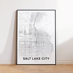 May include: Black and white line art map print of Salt Lake City, Utah. The print is framed in a black frame and has the city name and state printed below the map.