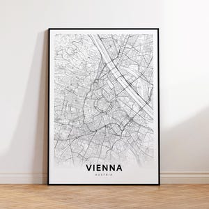 May include: A black framed print of a detailed map of Vienna, Austria. The map is in black and white, showing the city's streets and landmarks. The word "VIENNA" is printed in a bold, sans-serif font at the bottom, with "AUSTRIA" below it.