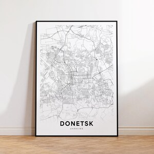 Puede incluir: Una impresión enmarcada en blanco y negro del mapa de Donetsk, Ucrania. El mapa detalla las carreteras e infraestructuras de la ciudad. El nombre de la ciudad y el país están impresos en la parte inferior.