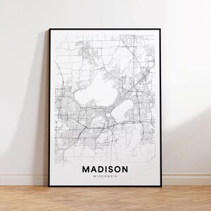 Puede incluir: Un mapa en blanco y negro enmarcado de Madison, Wisconsin. El mapa detalla las carreteras, vías fluviales y el diseño urbano de la ciudad. El nombre de la ciudad está impreso en negrita, con una fuente sans-serif en la parte inferior.