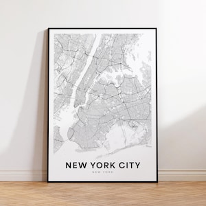 Pode incluir: Um mapa em preto e branco emoldurado da cidade de Nova York, com um layout detalhado das ruas. O texto "NEW YORK CITY" e "NEW YORK" é impresso em preto na parte inferior. O mapa é exibido em um piso de madeira.