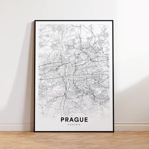 May include: A black framed print of a detailed map of Prague, Czechia. The map is in black and white, showing streets, buildings, and the Vltava River. The word "PRAGUE" is printed in bold, with "CZECHIA" below it.