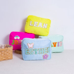 May include: Four colorful zippered pouches with embroidered names: Lean, Josh, Esther, and David. The pouches are made of a soft, textured fabric and have a variety of embellishments, including butterflies, flowers, and rainbows.