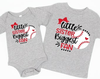 Può includere: Due top grigi a tema baseball. Uno è una t-shirt a maniche corte, l'altro un body per neonati. Entrambi presentano la scritta "Little Sister Biggest Fan" con una grafica di baseball e un fiocco rosso.