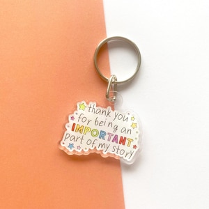May include: A clear acrylic keyring with a silver metal ring. The keyring features a colourful design with the text "thank you for being an IMPORTANT part of my story". The background is orange and white.