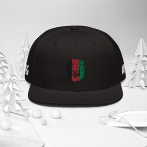 Op de afbeelding: Zwarte fitted baseballcap met een geborduurd leeuwenhoofd in zwart en rood. Het leeuwenhoofd is in tweeën gedeeld, de linkerzijde is zwart en de rechterzijde rood en groen.