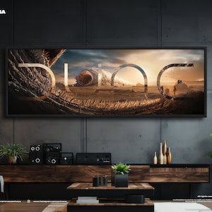 Pode incluir: Uma obra de arte emoldurada com a palavra "DUNE" em uma fonte estilizada, ambientada em uma paisagem desértica com uma criatura semelhante a um verme. A obra de arte é exibida acima de um console de mídia de madeira com alto-falantes e plantas.