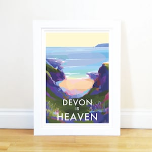 Pode incluir: Uma ilustração colorida de uma cena de praia em Devon, Inglaterra. A imagem mostra uma enseada com uma praia de areia e água azul. O texto "Devon is Heaven" está impresso abaixo da imagem.