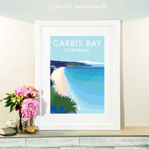 May include: A framed print of a colorful illustration of Carbis Bay, Cornwall. The image shows a beach with white sand and turquoise water. The text "Carbis Bay Cornwall" is printed in white on a light blue background.