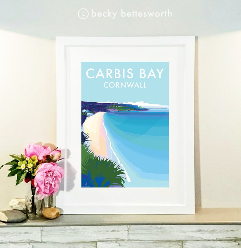 May include: A framed print of a colorful illustration of Carbis Bay, Cornwall. The image shows a beach with white sand and turquoise water. The text "Carbis Bay Cornwall" is printed in white on a light blue background.
