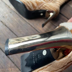 May include: Tan and brown patterned ankle boots with gold-colored heels. The boots have a pointed toe and a zipper on the side. The heels are approximately 3 inches high.