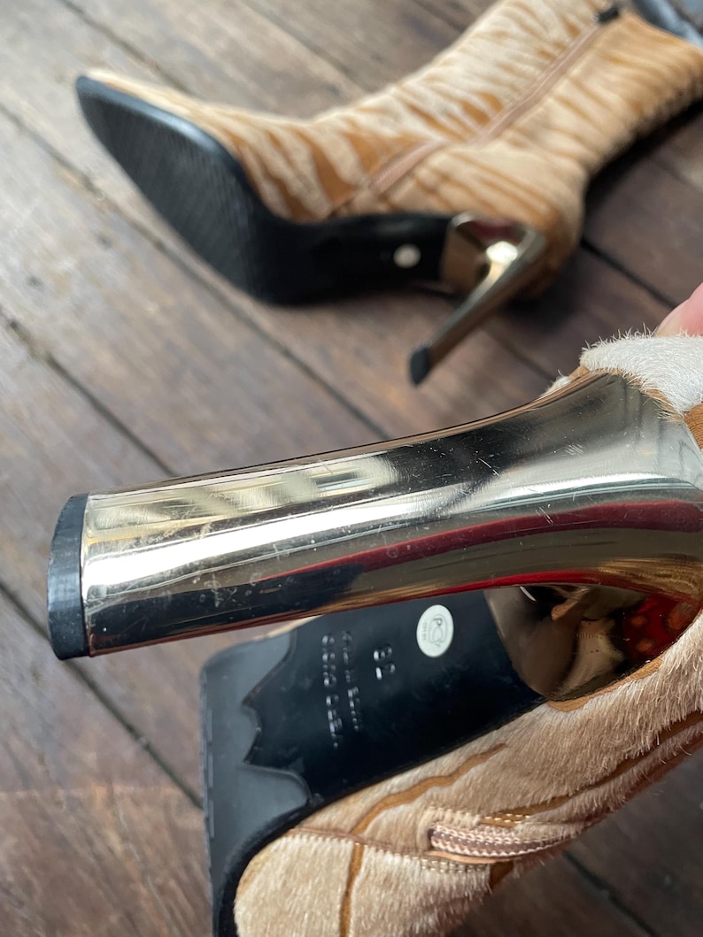 May include: Tan and brown patterned ankle boots with gold-colored heels. The boots have a pointed toe and a zipper on the side. The heels are approximately 3 inches high.