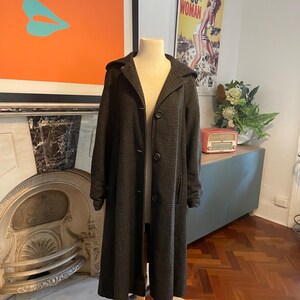 May include: A long, brown and black plaid coat with a hood and button closure. The coat is on a mannequin and is displayed against a white wall.