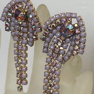 Puede incluir: Un par de pendientes vintage con un diseño en cascada. Los pendientes presentan una montura de metal dorado, adornada con cuentas de color lavanda y pedrería iridiscente multicolor. La piedra central es un gran cristal iridiscente.