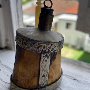 Puede incluir: Una pequeña botella antigua de hueso y plata con un tapón decorativo. La botella es marrón y tiene detalles plateados. El tapón es de marfil y tiene un anillo plateado.