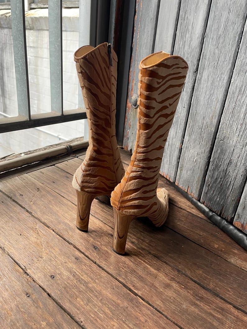 May include: A pair of knee-high boots with a tiger stripe pattern in shades of tan and brown. The boots have a high heel and a zipper closure. The boots are made of a soft, textured material.