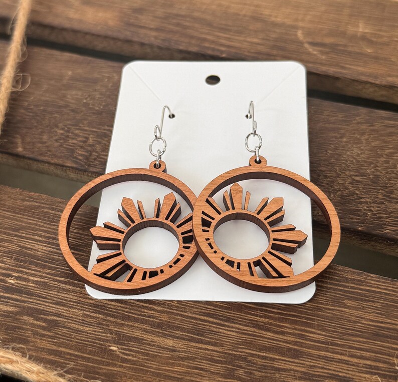 May include: A pair of wooden earrings with a sunburst design. The earrings are brown and have a silver hook.