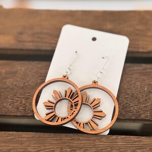 May include: A pair of wooden earrings with a sunburst design. The earrings are brown and have a silver hook.