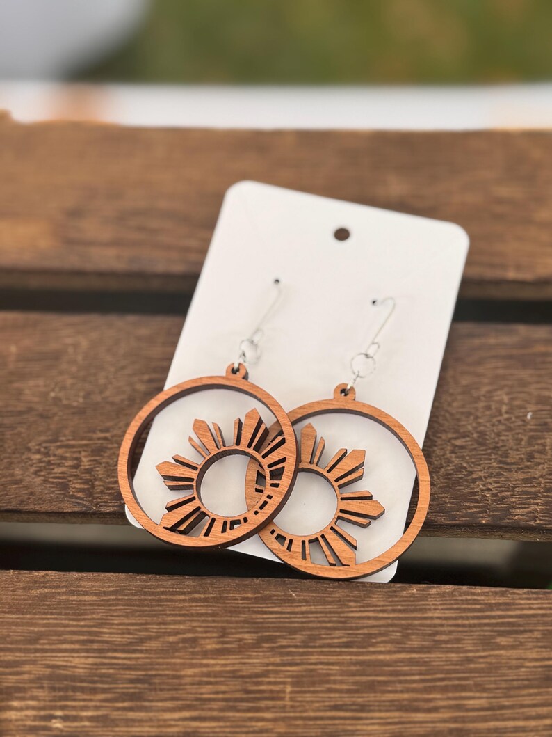 May include: A pair of wooden earrings with a sunburst design. The earrings are brown and have a silver hook.