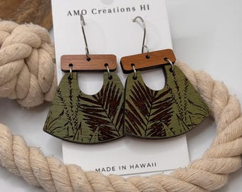 May include: A pair of green wood earrings with a brown wood accent and a leaf pattern. The earrings are hanging from silver hooks. The earrings are labeled "AMO Creations HI" and "MADE IN HAWAII".