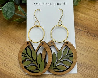May include: A pair of wooden earrings with a green leaf design and gold hoops. The earrings are on a white card with the text "AMO Creations HI".