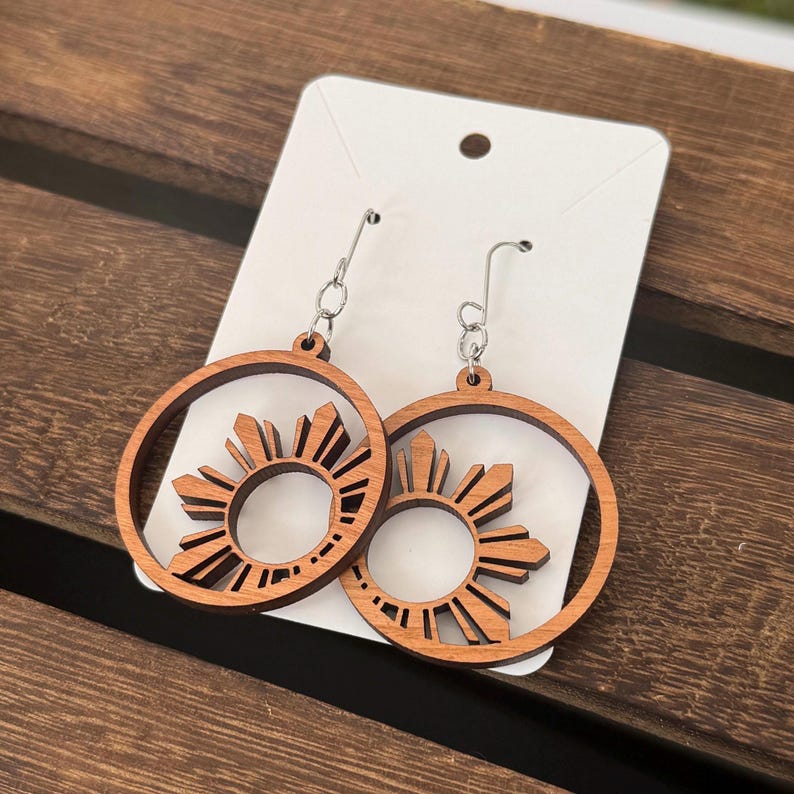 May include: A pair of wooden earrings with a sun design. The earrings are brown and have silver hooks.