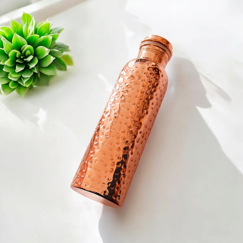May include: A copper water bottle with a hammered finish. The bottle has a rounded shape and a smooth, polished surface.