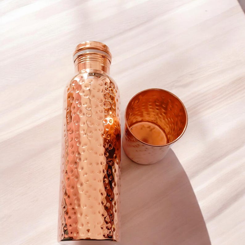 May include: A set of two copper water bottles with hammered texture. The bottles are a shiny copper color and have a round shape.