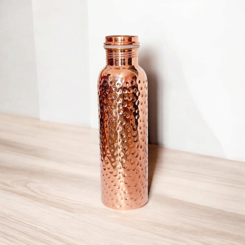 May include: A hammered copper water bottle with a copper lid. The bottle has a textured surface and is a light copper color.