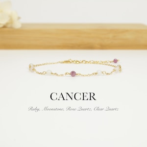 Puede incluir: Una delicada pulsera de cadena dorada con piedras preciosas rosas y blancas alternas. La palabra "CANCER" se muestra debajo de la pulsera, con las piedras preciosas identificadas como Rubí, Piedra Lunar, Cuarzo Rosa y Cuarzo Claro.