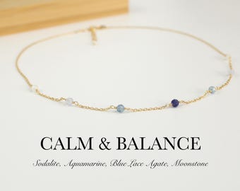 May include: A delicate gold chain necklace featuring small, spaced-out gemstone beads including sodalite, aquamarine, blue lace agate, and moonstone. The text CALM & BALANCE and Sodalite, Aquamarine, Blue Lace Agate, Moonstone is printed below.