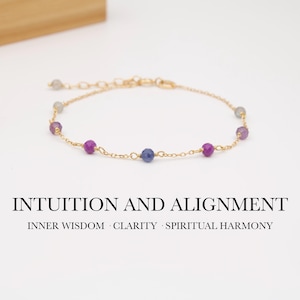 Op de afbeelding: Een delicate goudkleurige kettingarmband met kleine, gefacetteerde, ronde paarse en blauwe edelsteenkralen. De tekst INTUITION AND ALIGNMENT en INNER WISDOM CLARITY SPIRITUAL HARMONY staat onder het sieraad afgedrukt.