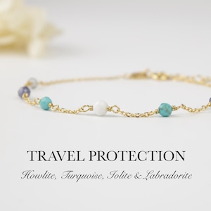 May include: A delicate gold chain bracelet adorned with turquoise, white, and purple beads. The bracelet is displayed on a white surface. Text on the image reads "TRAVEL PROTECTION" and lists the stones: Howlite, Turquoise, Iolite & Labradorite.