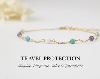 May include: A gold-toned chain bracelet featuring small, round beads in white, turquoise, and purple. The text TRAVEL PROTECTION Howlite, Turquoise, Iolite & Labradorite is printed below the jewelry piece, which has a delicate link design.
