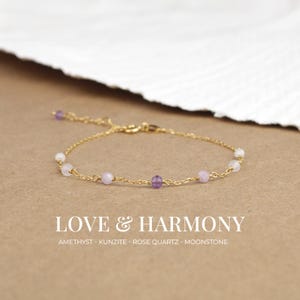Puede incluir: Un brazalete de cadena dorada con cuentas de amatista, kunzita, cuarzo rosa y piedra lunar. El brazalete tiene una cadena delicada y está adornado con pequeñas piedras preciosas de colores. El brazalete se llama "Love & Harmony".