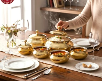 May include: A set of gold-toned, hammered metal serving bowls and lidded containers arranged on a wooden table. The collection includes various sizes of round bowls, some with matching lids, containing cooked rice and savoury dishes.